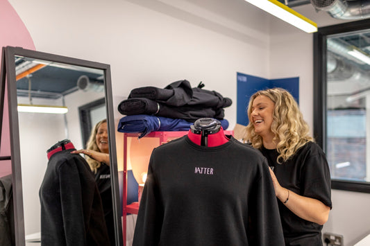 Gemma smiling beside a mannequin wearing a black MATTER sweatshirt inside a fashion studio with folded fabrics.