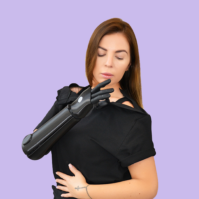Woman with prosthetic arm fastens WearMatter adaptive T-shirt with shoulder magnets on purple background.