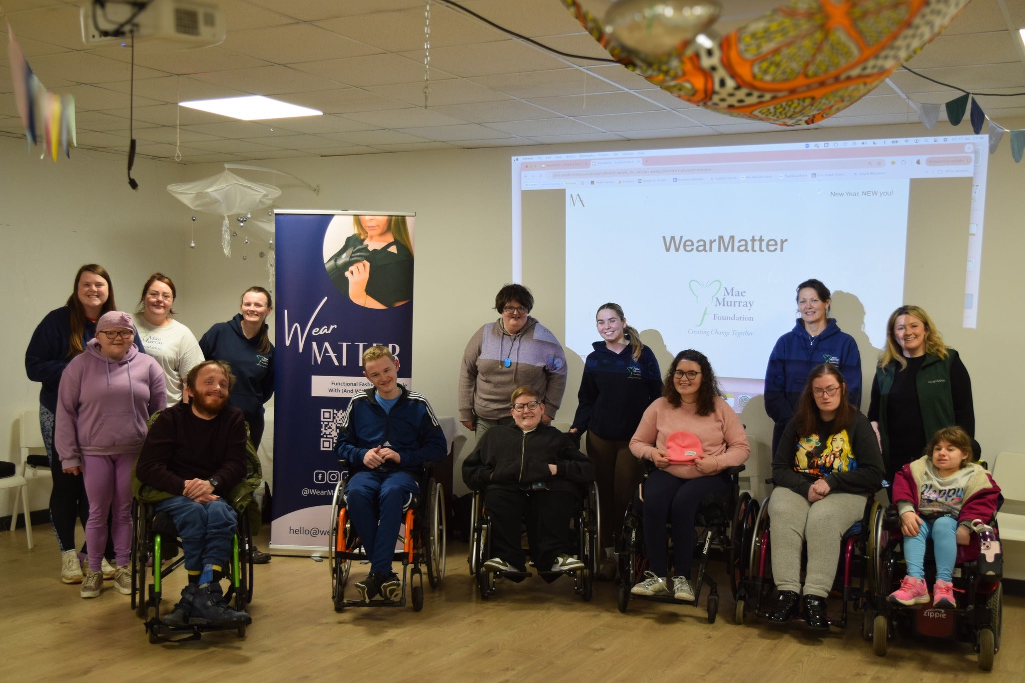 Group photo of WearMatter and Mae Murray Foundation members at an inclusive fashion workshop, in front of a WearMatter presentation screen